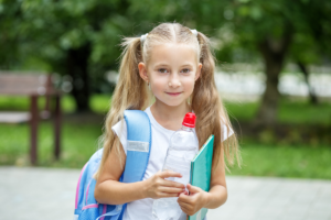 A young girl carrying a backpack and holding a water bottle, ready for her day ahead.