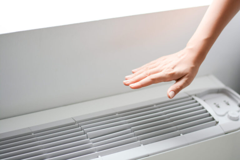 Hand over air conditioner checking to see if it's blowing warm or cool air