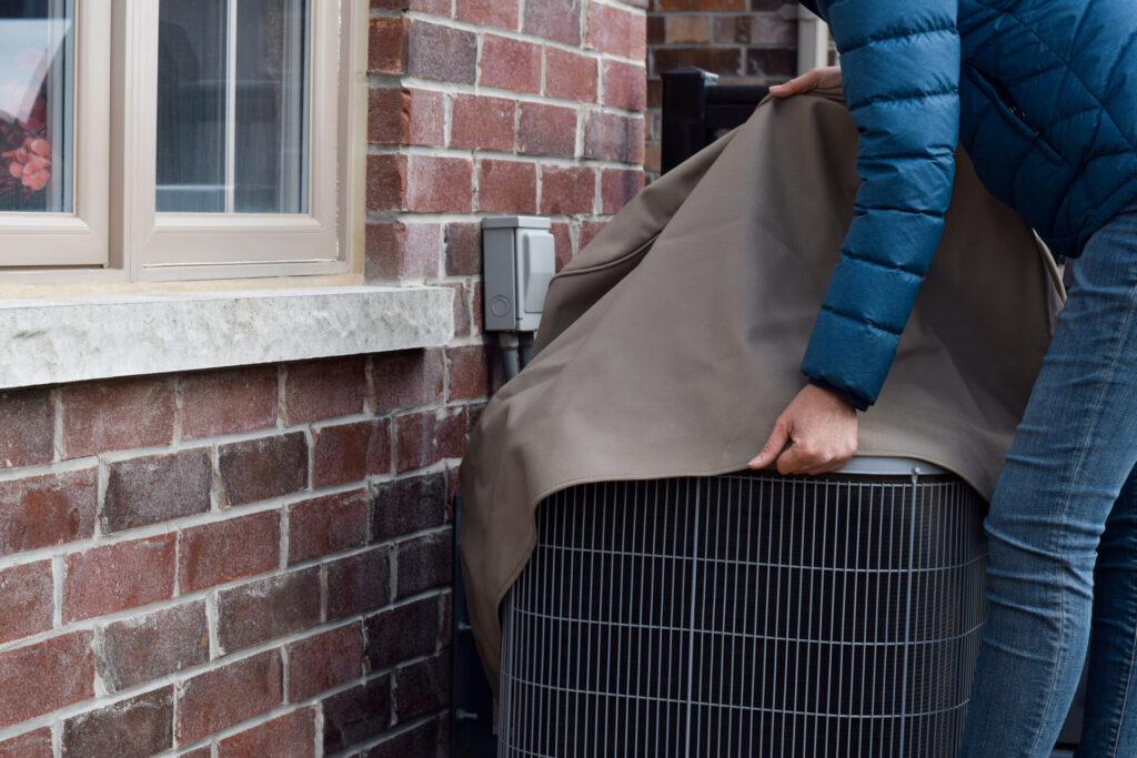 a homeowner covering their HVAC unit in preparation for winter