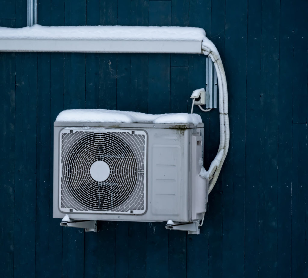 Heat pump mounted on the wall of a house and covered in snow on a cold winters day.