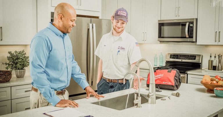 A plumber conversing with a homeowner in a kitchen after fixing the sink.
