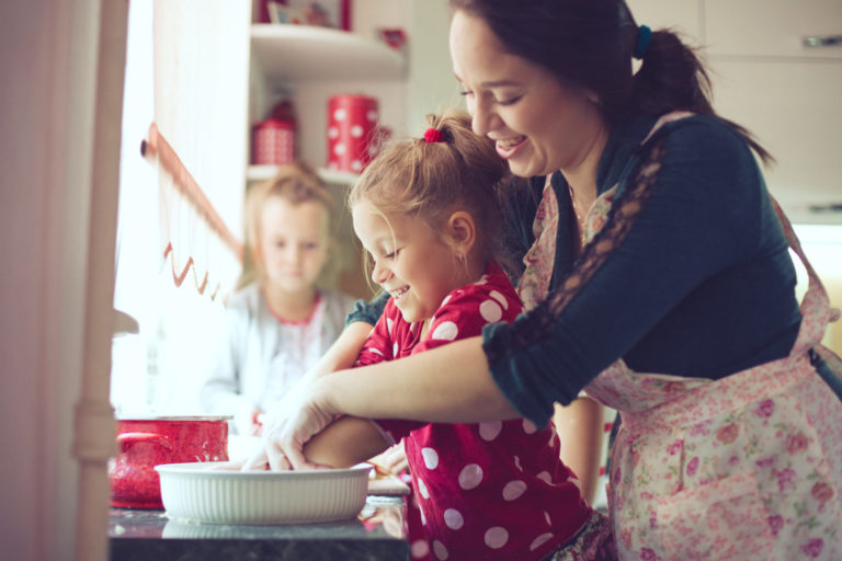 A woman and two children preparing food in a kitchen, creating a warm and familial atmosphere.