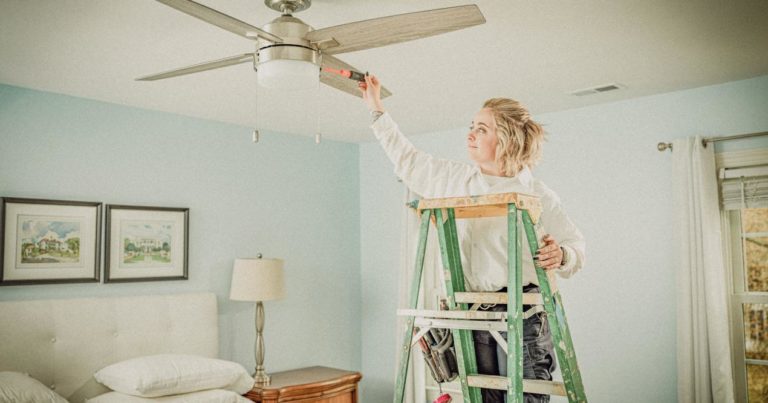 A woman on a ladder fixing a ceiling fan.