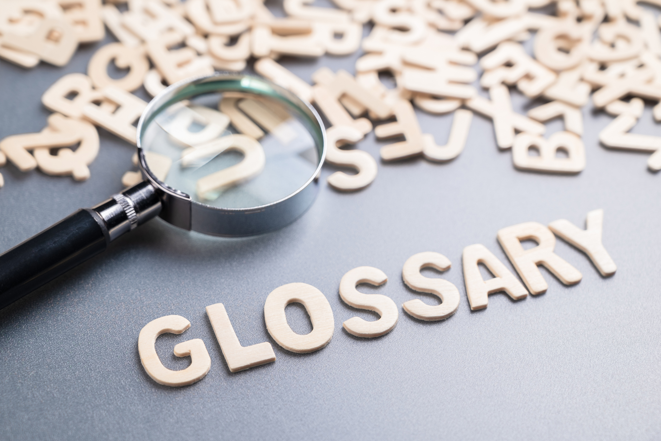 Glossary spelled out with letters surrounded by small wooden alphabets with a magnifying glass
