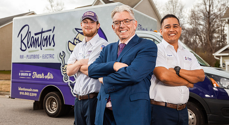 Three employees stand in front of a company van. 