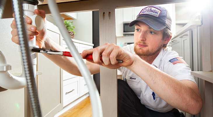 Blanton's plumber repairing pipes below a kitchen sink